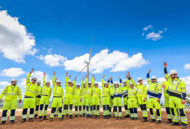 Ansatte løfter armene i været foran en vindmølle