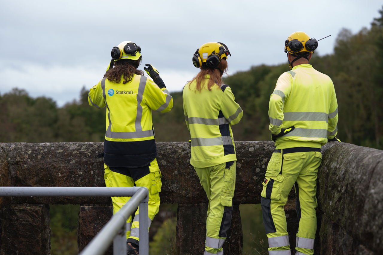 Tre ansatte i verneutstyr ser utover en utsikt